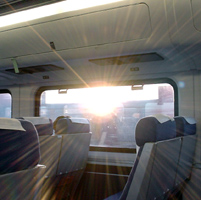 Amtrak California cars have large windows, padded seats, and overhead luggage bins. This picture looks out, toward the sunrise.