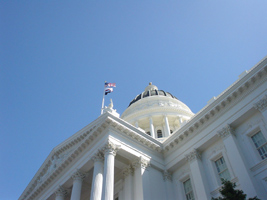 The California State Capitol is an ornate white building with columns and a rounded dome. Flags fly from a pole over the entrance.
